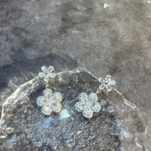 Close-up of flower drop earrings featuring sparkling zircon crystals on a glass plate