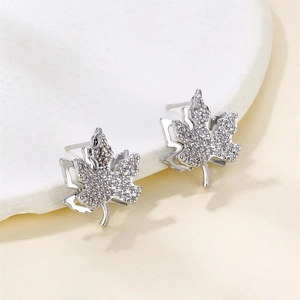 Boucles d'oreilles feuille d'érable en argent avec zircons sur fond beige élégant