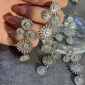 Detailed view of silver flower drop earrings with white crystals held by hand