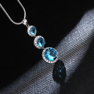 Macro shot of silver halo pendant featuring three tiered round blue topaz stones