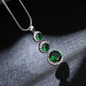 Close-up of elegant silver necklace with three graduated green stones and pave diamonds