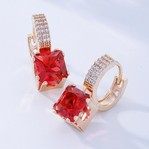 Gros plan de boucles d'oreilles dorées avec pierre rouge carrée et cristaux pavés