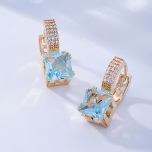 Détail de boucles d'oreilles carrées en pierres bleu clair avec finition or et diamants