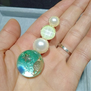Gros plan d'une pince à cheveux verte motif galaxie avec perles blanches à la main