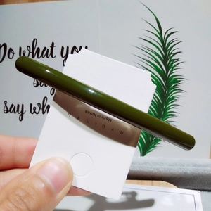 Détail de la pince à cheveux vert foncé brillante sur carte, tenue à la main devant un décor mural