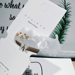 Detail of a white marble acetate cat hair clip displayed on a branded jewelry card