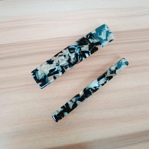 Detail of two black and white marble pattern hair clips on a light wood background