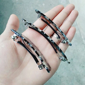 Three acetate hair clips with black and white marble pattern shown in a hand