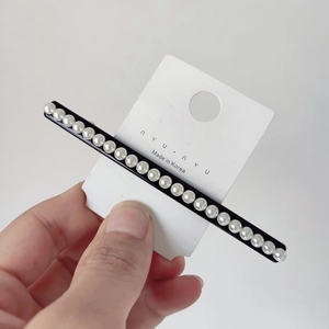 Detailed macro view of minimalist black pearl hair clip with 20 white pearls on a paper card