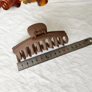 Détail de la grande pince à cheveux mate marron de 11 cm à côté d'une règle métallique