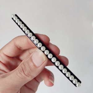 Detail view of a long black spring hair clip with elegant white pearls held in hand