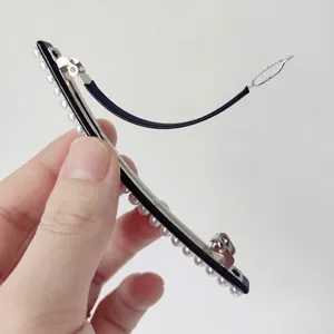 Minimalist black hair clip with white pearls and silver metal spring buckle held by hand