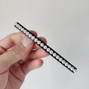 Detail showing hand holding a minimalist black spring clip with white pearls
