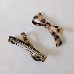 Detail view of tortoiseshell resin bow hair clips with metal spring bases on white stone