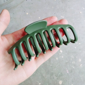 Détail d'une grande pince à cheveux mate vert foncé avec design multi-dents pour fixation