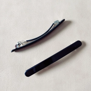 Detail of two glossy black spring hair clips showing the front surface and metal back