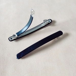 Detail of black glossy spring hair clip with silver metal structure on beige background