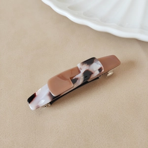 Macro shot of minimalist brown and tortoiseshell pattern acetate hair clip on beige background