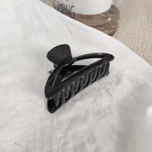 Détail d'une pince à cheveux noire brillante géométrique avec texture en spirale sur tissu