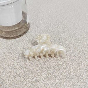 Dettaglio ravvicinato della molletta in acetato con texture marmo crema lucida