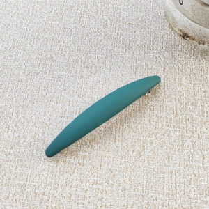 Detail of matte dark green hair clip showing its sleek curved shape and metal fastener
