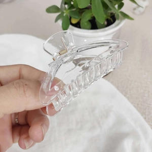 Détail d'une pince à cheveux transparente en forme de cœur avec ressort doré et logo