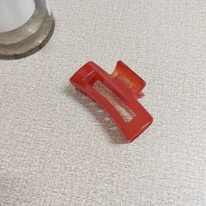 Detail view of a translucent red jelly resin hair claw clip on a textured beige surface