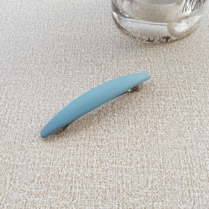 Detailed macro view of matte Morandi blue spring hair clip on a textured beige surface