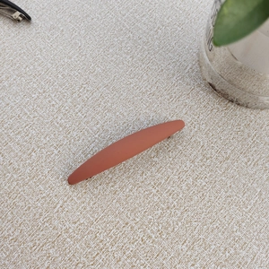 Close-up of matte terracotta rectangular hair clip with frosted texture on beige fabric