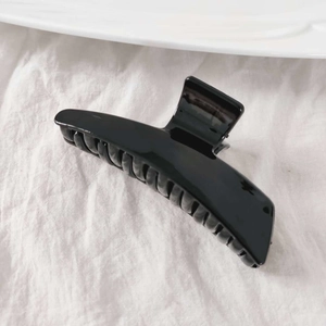 Detail view of large glossy black hair claw clip on white linen fabric background