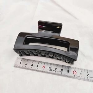 Measurement photo showing an 11cm large black hair claw clip on a white fabric background