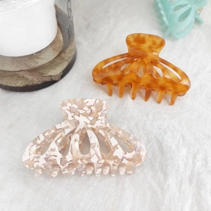 Detail view of tortoiseshell and marbled acetate hair claws on a linen cloth background