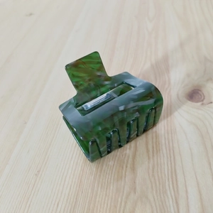 Macro shot of marble textured dark green hair claw clip with metal spring on wood surface