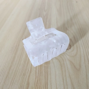 Detail of a large square marble-patterned acetate hair claw clip on a light wooden background