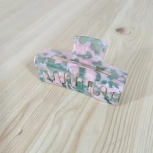 Nahaufnahme einer Haarklammer aus Acetat in Rosa und Grün mit Marmormuster auf Holz