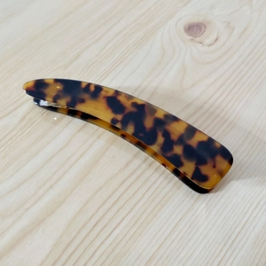 Close-up of a large curved leopard print tortoiseshell banana hair clip on wood