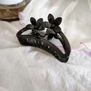 Détail d'une pince à cheveux noire brillante avec fleurs en résine sur tissu blanc gaufré