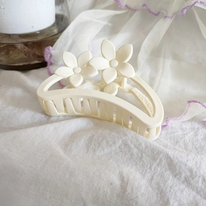 Détail de la pince à cheveux fleur crème en résine sur un fond de tissu blanc
