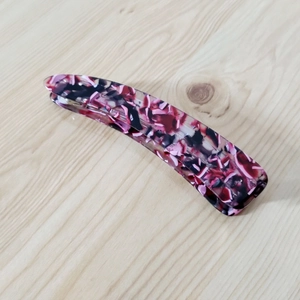 Close-up of elegant banana hair clip with red and white marble patterns on wood