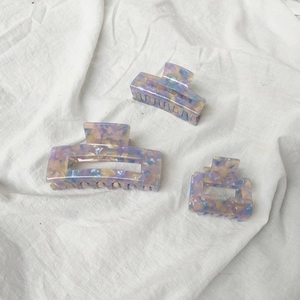 Close-up of three acetate hair claws in pastel marble patterns on soft white fabric