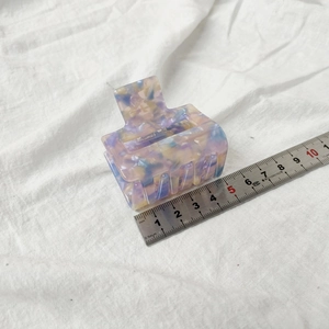 Detail view of a square marble pattern hair claw clip with a scale ruler for size