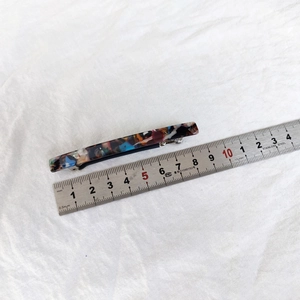 Detail view of a 6.5cm acetate spring hair clip with colorful marble pattern and ruler