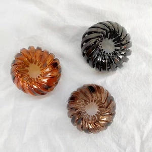 Three expandable bird nest hair clips in amber, coffee and black on white fabric