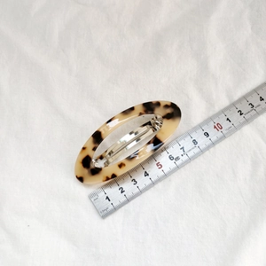 Vue détaillée d'une barrette ovale de 7 cm en écaille sur un tissu blanc texturé