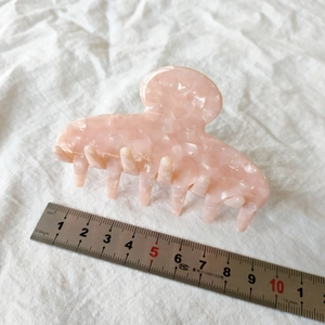 Detailed macro view of 9cm pink marble acetate hair claw clip on white linen fabric