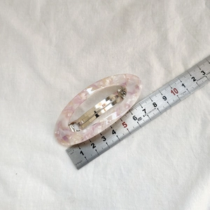 Vue macro d'une pince à cheveux ovale marbrée rose montrant une longueur de 6,5 cm sur règle