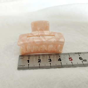 Détail d'une pince à cheveux en acétate rose marbré de 5 cm sur tissu blanc