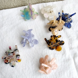 Detail view of eight colorful floral hair claws in acetate and resin on white fabric