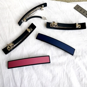 Gros plan de barrettes à cheveux en résine mate noire, bleue et rose sur tissu blanc
