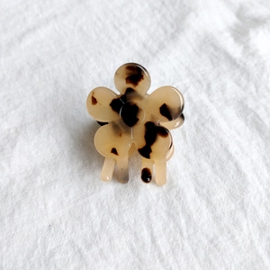 Detailed top view of a small tortoiseshell flower hair claw clip on white fabric